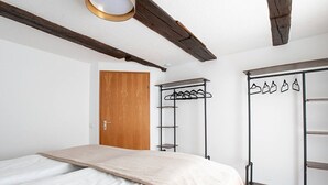 A bedroom with a bed, a wooden door, a metal coat rack, and a wardrobe with hanging items.