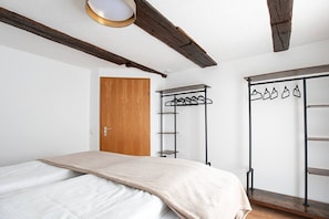 A bedroom with a bed, a wooden door, a metal coat rack, and a wardrobe with hanging items.