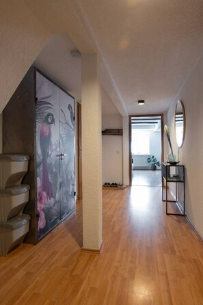 A hallway with wooden flooring, a mirrored cabinet, and a door with a tropical mural.