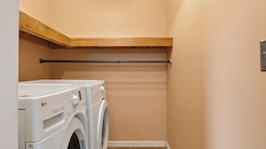 Uma lavanderia com duas máquinas de lavar roupa brancas LG Direct Drive e uma prateleira de madeira acima.