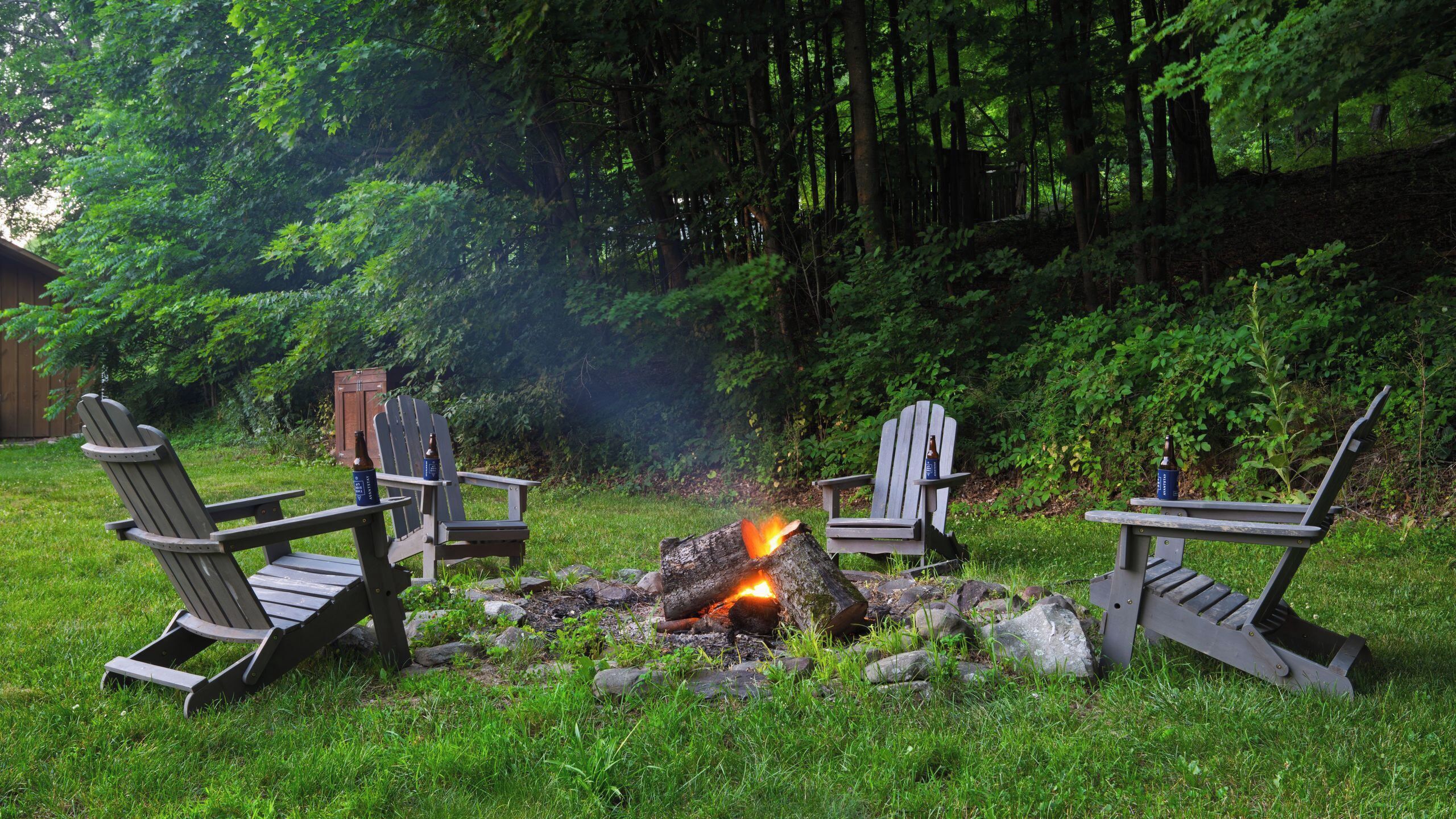 A campsite with three Adirondack chairs around a campfire.