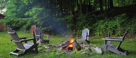 A campsite with three Adirondack chairs around a campfire.