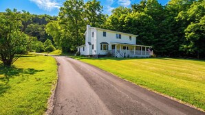 A two-story house with a porch, surrounded by a well-maintained lawn and trees. - Ohana Nature Escape by Avantstay Creekside + Firepit + Grill Waterfall + Beaver Pond Walks (Catskill)