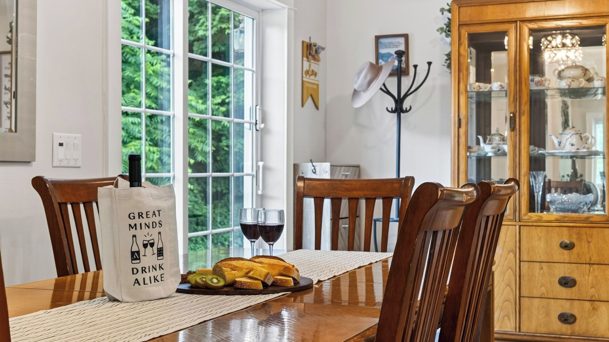 Uma sala de jantar com uma mesa de madeira, cadeiras, um armário de vidro e uma janela com vista para o verde.