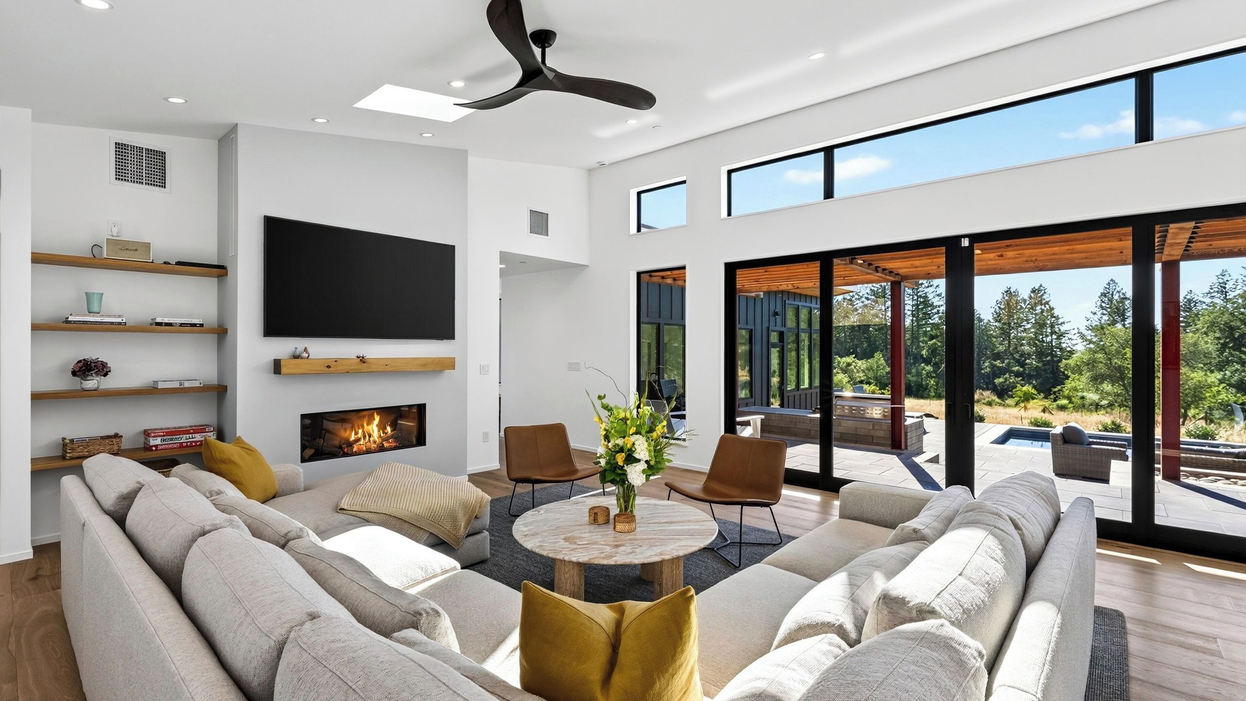 A modern living room with a fireplace, a large flat-screen TV, and a view of the outdoors.