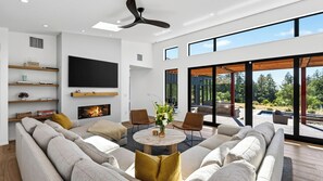 A modern living room with a fireplace, a large flat-screen TV, and a view of the outdoors. - Olive & Oak by Avantstay 75-ft Lap Pool + Hot Tub + Sauna 40 Private Acres (Glen Ellen)