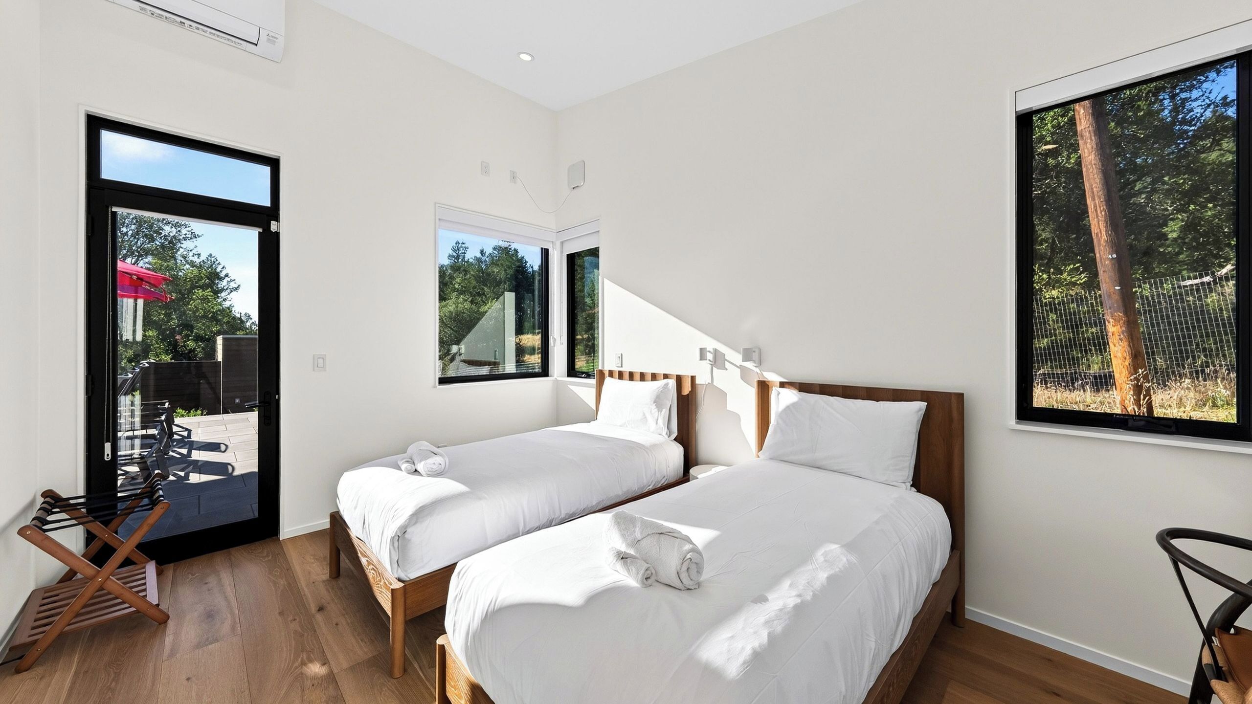 A modern bedroom with two beds, a wooden floor, and large windows.