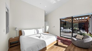 Ein modernes Schlafzimmer mit einem großen Bett, einem Nachttisch, einer Lampe und Blick auf eine Terrasse.