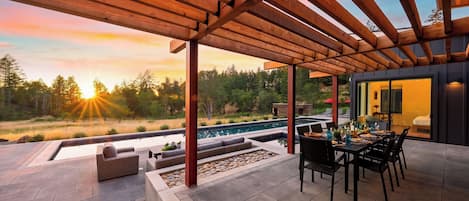 Un espacio al aire libre techado con piscina, asientos y vistas al atardecer.