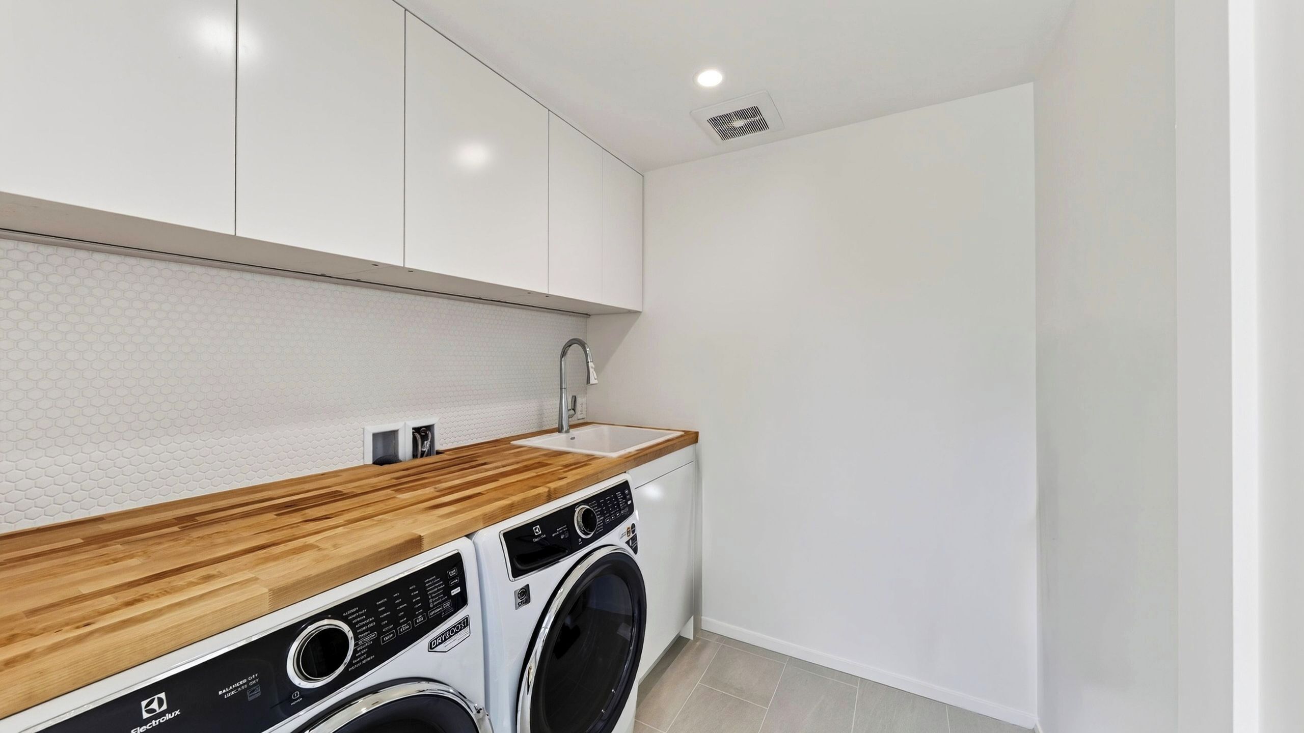 A modern laundry room with a washing machine, a sink, and a wooden countertop.