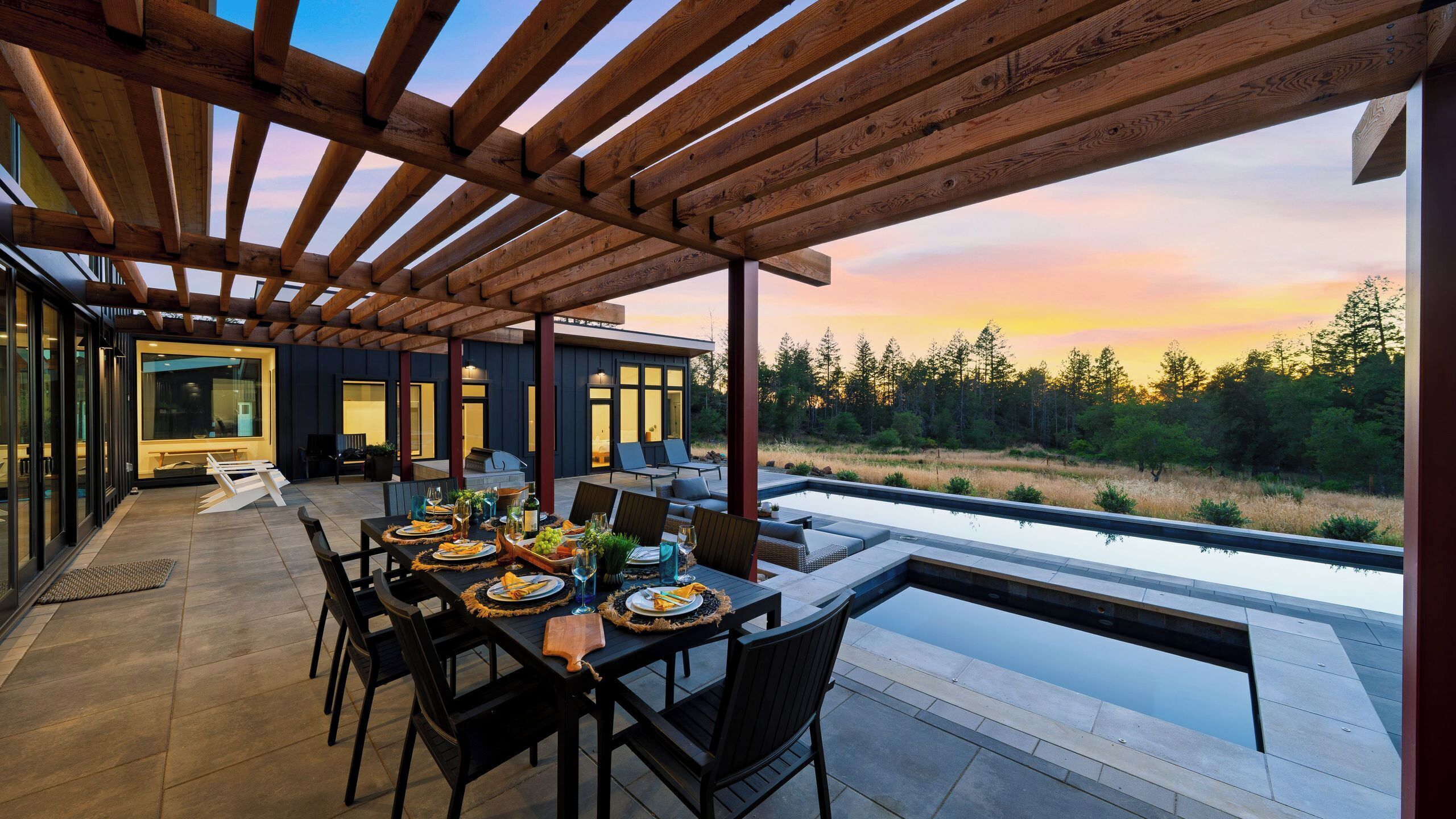 An outdoor dining area with a view of a forest and a pool.