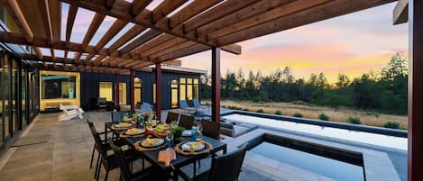 Un área de comedor al aire libre con vistas a un bosque y una piscina.