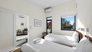 Ein Hotelzimmer mit zwei Betten, einem Fenster mit Blick ins Freie, einer Tür, die auf einen Balkon führt, und einem Schild an der Wand.