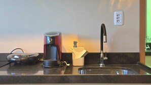Una encimera de cocina con una cafetera, un hervidor, una taza y un lavabo.