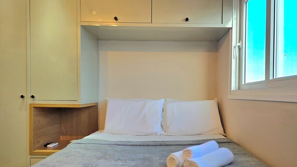 Un dormitorio con cama, almohadas, una mesita de noche de madera y una ventana.
