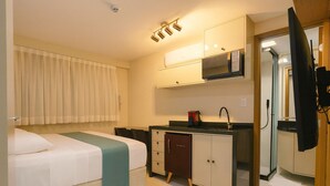 Habitación de hotel compacta con cama, kitchenette, microondas y un mueble pequeño.