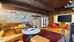 A cozy living room with a stone wall, wooden furniture, a marble coffee table, and a television. - Ashokan Acres by Avantstay Private 125-acre Retreat Pond + Hot Tub + Sauna + Trails (Kingston)