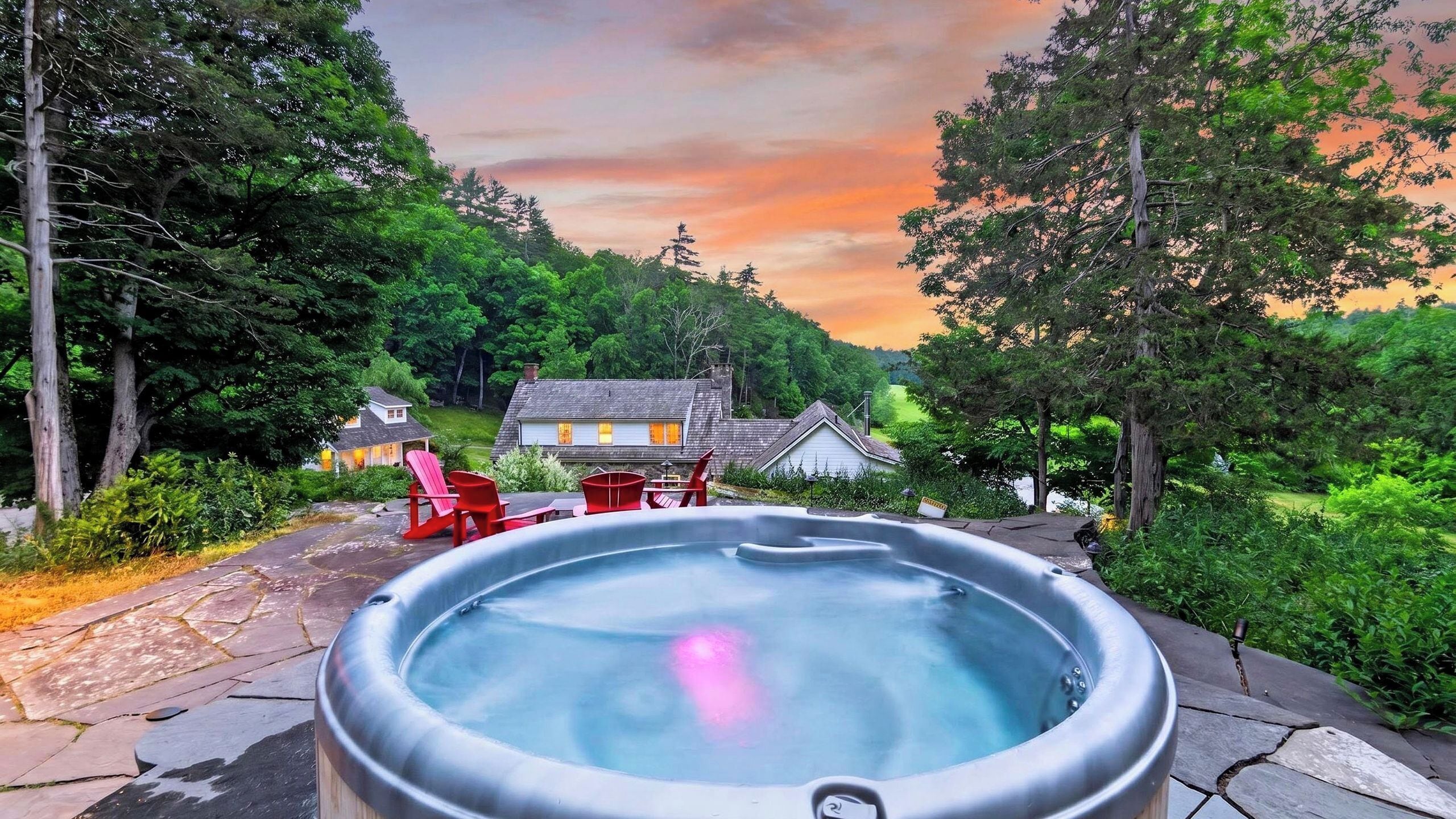 A hot tub surrounded by lush greenery and a house with a sloped roof.