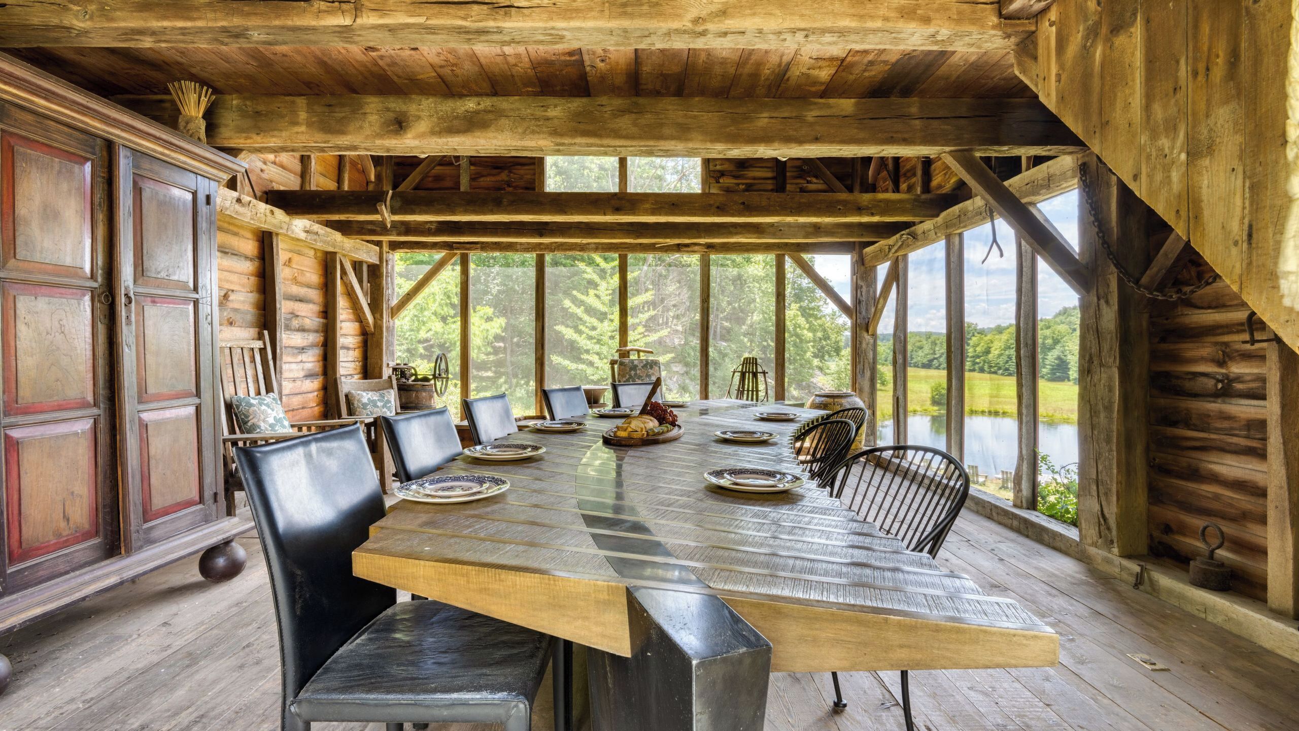 A rustic wooden dining area with a long table set for a meal, surrounded by chairs.
