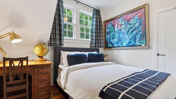 Ein Schlafzimmer mit einem Bett, einem Schreibtisch mit Globus, einem Gemälde und einem Fenster mit Vorhängen.