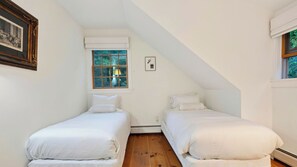 Quarto com duas camas de solteiro, janela com vista para o verde e um quadro na parede.