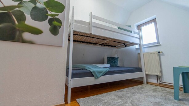 Une chambre avec un lit superposé, une fenêtre, un radiateur et une plante.