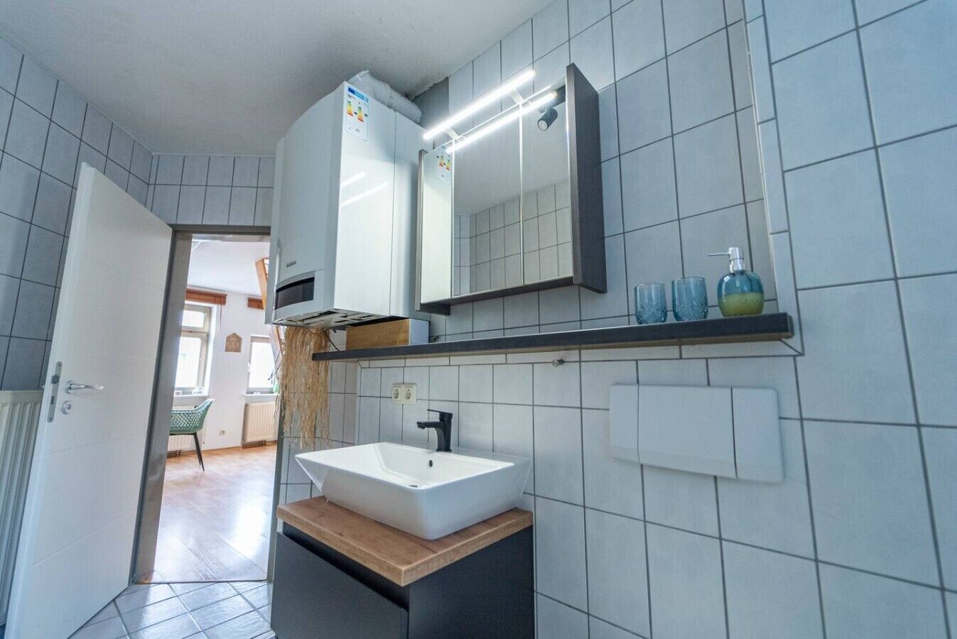 A modern bathroom with a white sink, a mirror above it, and a shelf with toiletries.