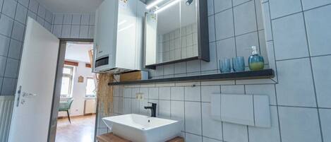 A modern bathroom with a white sink, a mirror above it, and a shelf with toiletries.