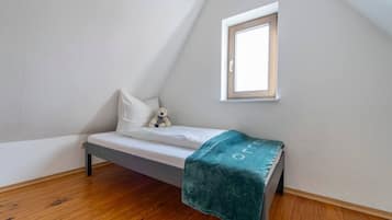 Ein kleines Zimmer mit einem Einzelbett, schrägen Wänden, einem Fenster und Holzboden.