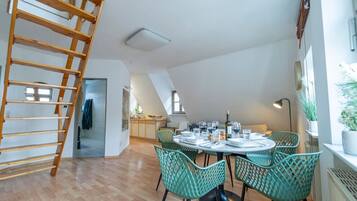 Ein Loft-Zimmer mit einer Holzleiter, einem Esstisch mit Stühlen und einer Küchenzeile im Hintergrund.