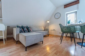 Ein modernes Wohnzimmer mit einer Couch, einem Esstisch mit Stühlen, einer Lampe und einer Wanduhr.