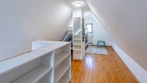 Un petit grenier étroit avec un plancher en bois, des étagères blanches et un petit tabouret.
