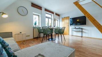 Ein modernes Wohnzimmer mit Essbereich, Fernseher und einer Wanduhr.