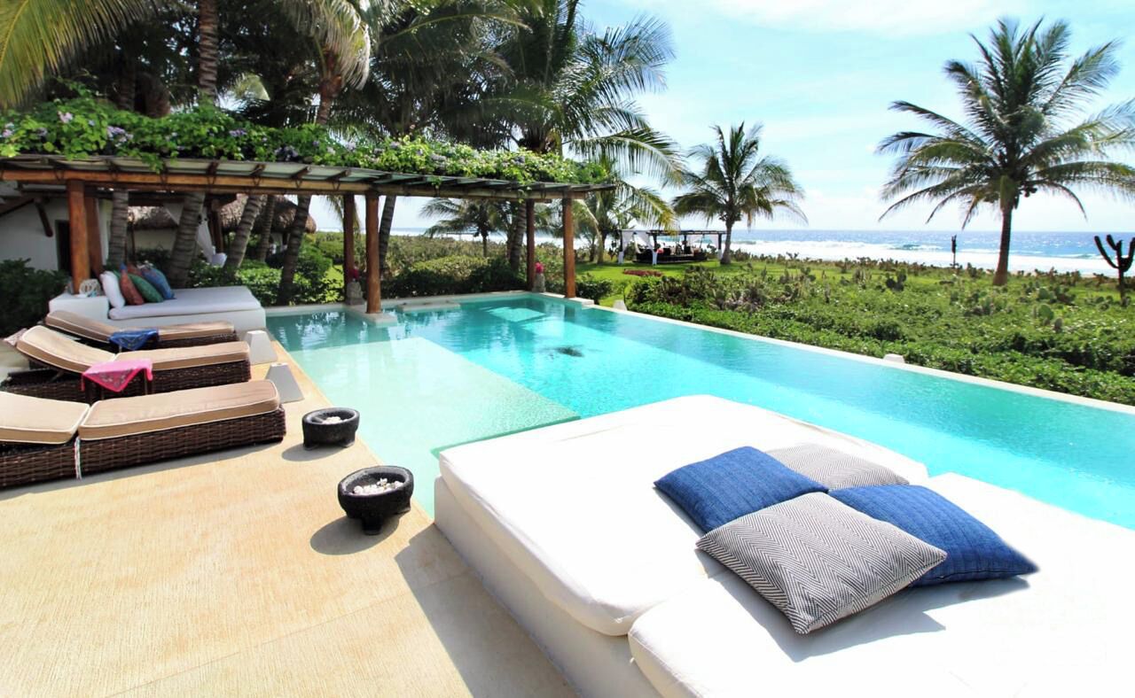 Ein Poolbereich mit Liegestühlen und einer Pergola, mit Blick auf einen Strand.