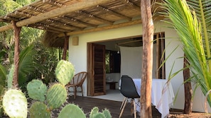 Un espacio al aire libre cubierto con mesa y sillas, una pérgola de madera y una planta de cactus.