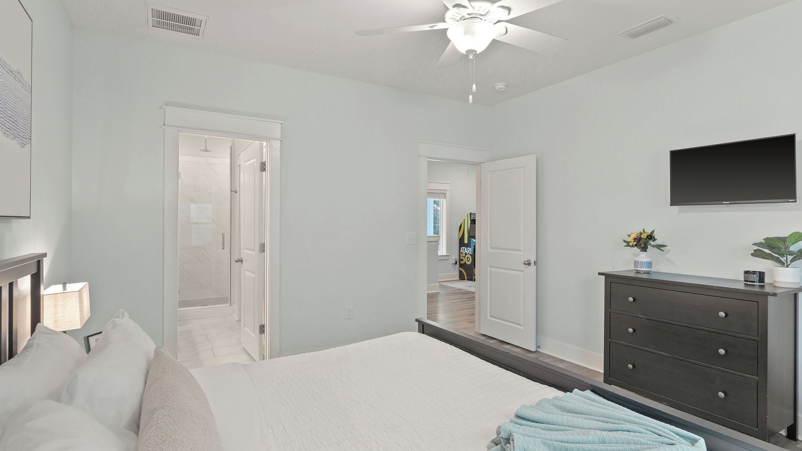 A bedroom with a bed, a dresser, a TV, and a ceiling fan.
