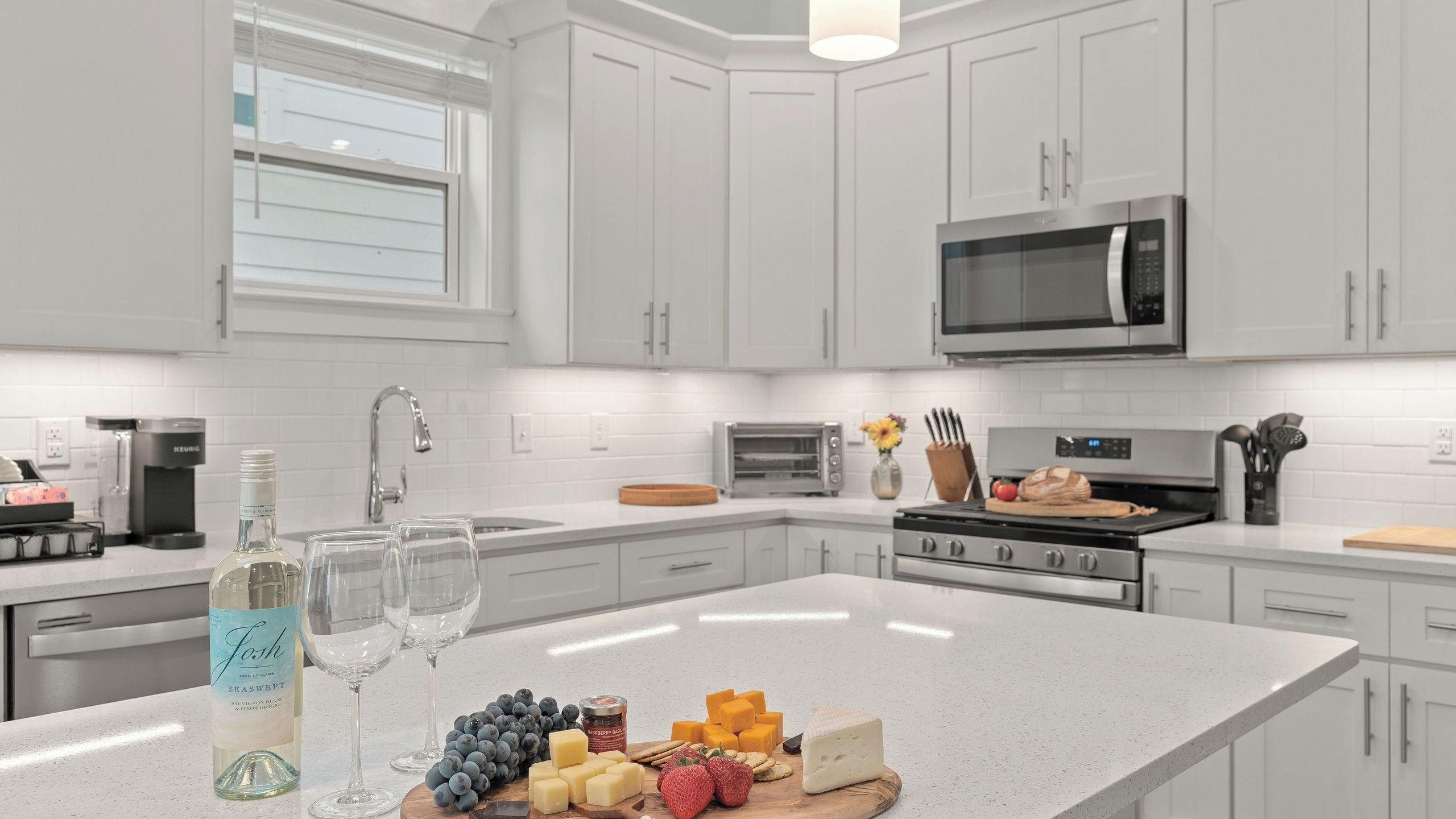 Una cocina moderna con muebles blancos, microondas integrado y una isla central con alimentos.