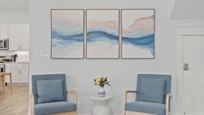 A modern living room with two armchairs, a small side table with a vase of flowers, and a kitchen in the background. - Serene on 30A by Avantstay Golf Cart + Pool + Game Room Steps to Beach (Santa Rosa Beach)