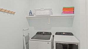 A laundry area with two washing machines, a drying rack, and a shelf with folded towels and a basket. - Serene on 30A by Avantstay Golf Cart + Pool + Game Room Steps to Beach (Santa Rosa Beach)