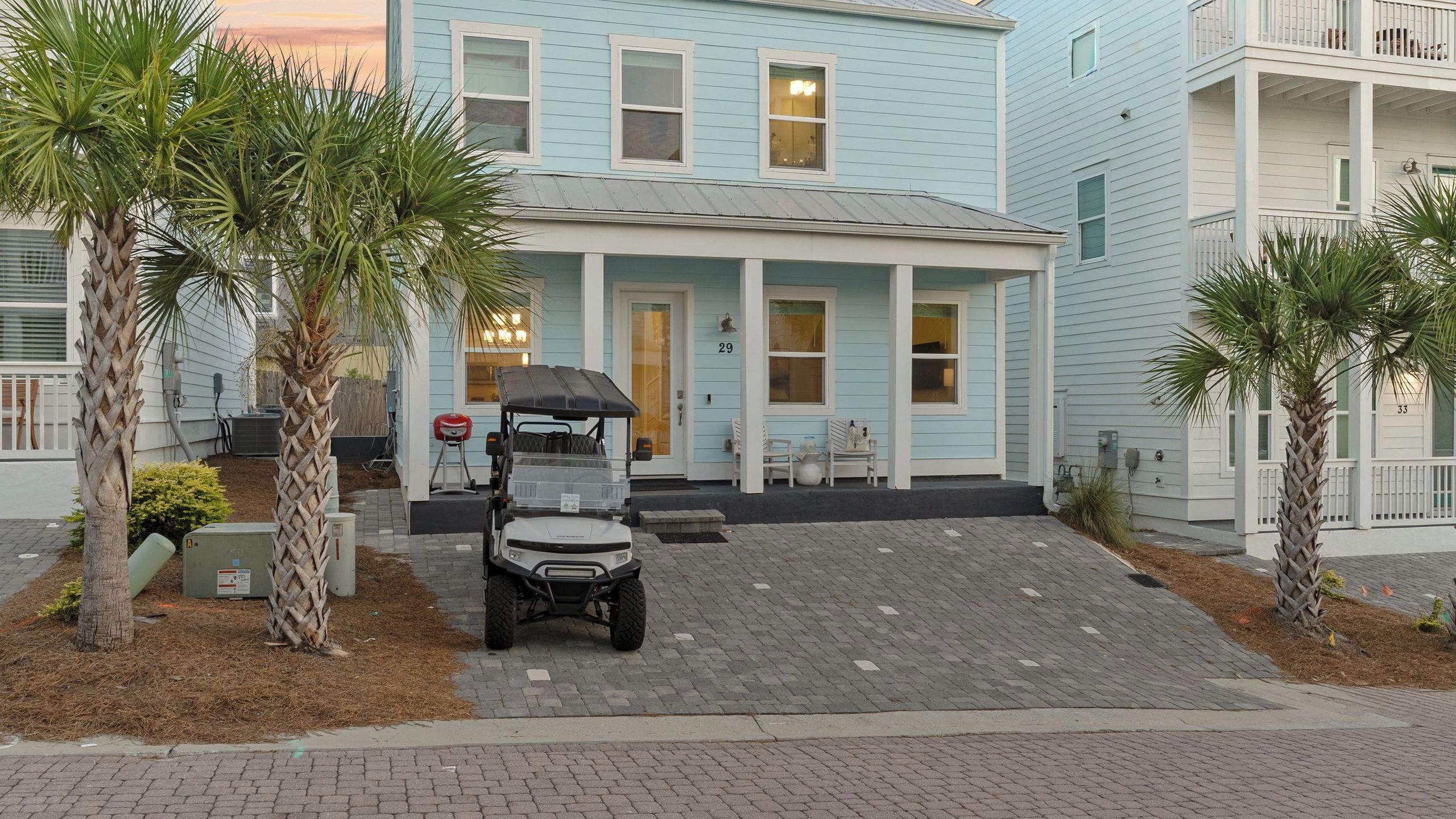 A light blue building with a covered porch, a golf cart, and palm trees.