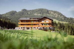 Un hotel de varios pisos con fachada de madera, situado en una zona montañosa y vistas a un bosque denso.