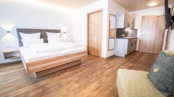 A modern hotel room with a wooden bed, a kitchenette, and a seating area.