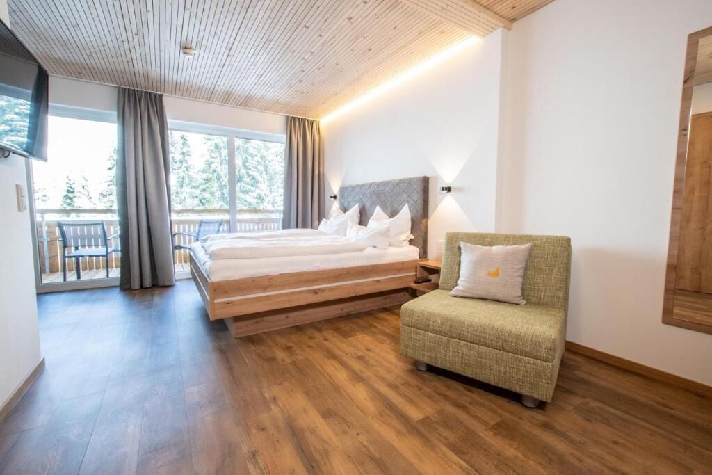 A bedroom with a bed, a green armchair, and a balcony with a view.
