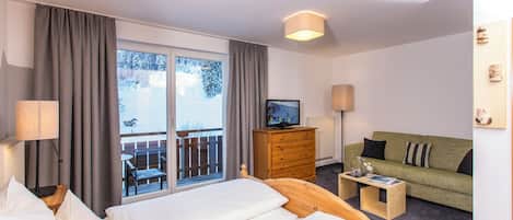 A hotel room with a bed, a sofa, a TV, and a view of a snowy outdoor area.