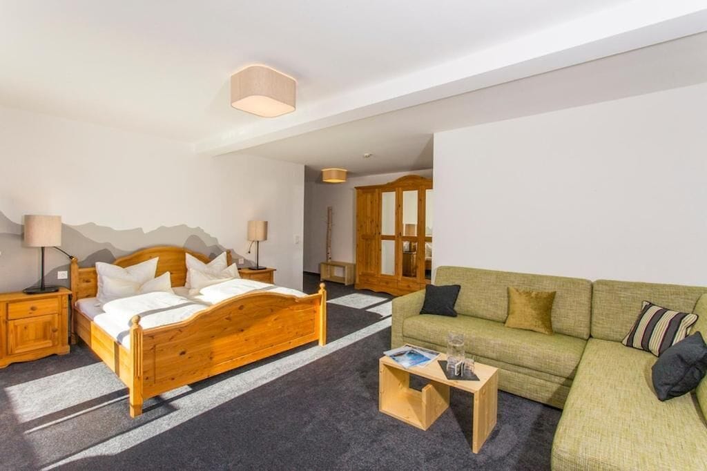 Ein Zimmer mit einem hölzernen Bett, einem grünen Sofa, einem kleinen Holztisch und einer Lampe.