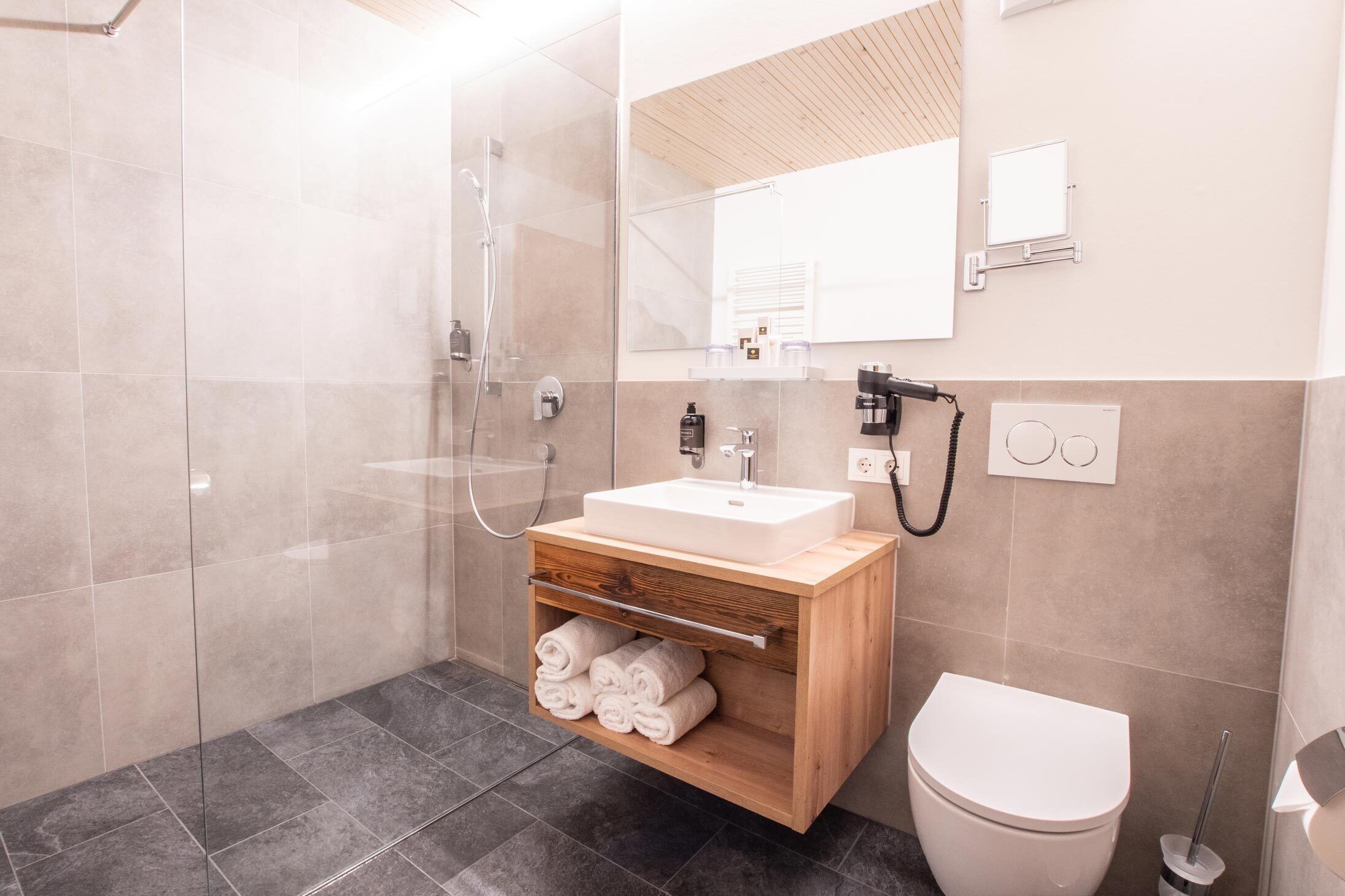 A modern bathroom with a glass-enclosed shower, a wooden vanity with a sink, and a toilet.