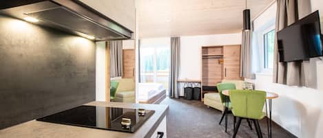 A modern kitchen with a built-in stove, a dining area with green chairs, and a flat-screen TV mounted on the wall.