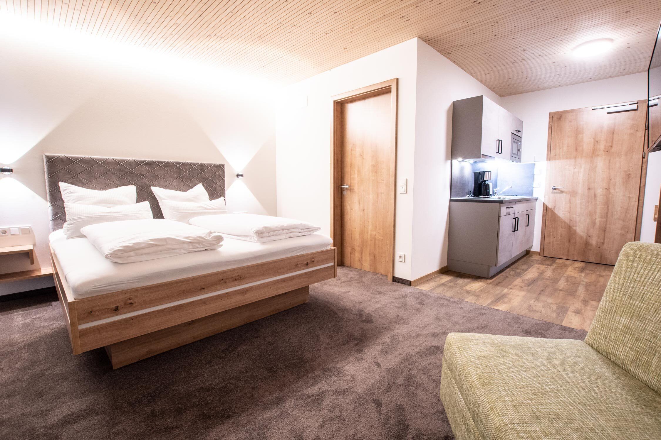 Ein Schlafzimmer mit einem Bett, einer kleinen Küchenzeile und einem grünen Sessel.