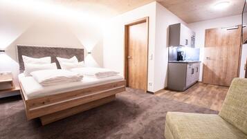 Ein Schlafzimmer mit einem Bett, einer kleinen Küchenzeile und einem grünen Sessel.