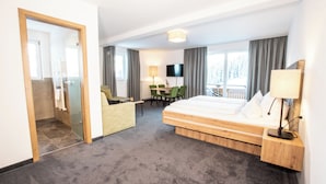 Habitació d'hotel amb llit, escriptori, cadira, televisió i finestra amb cortines.